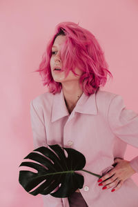 Young woman holding leaf while standing against colored background