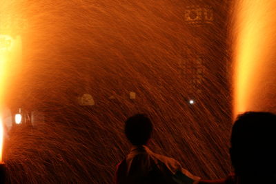 Rear view of people standing against illuminated orange sky