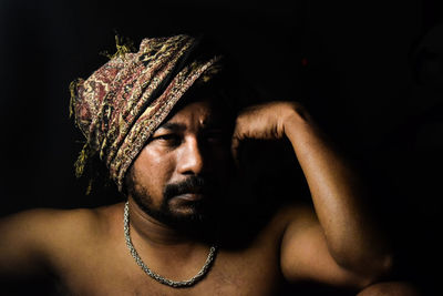 Close-up portrait of shirtless man against black background