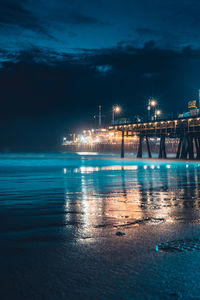 Illuminated city by sea against sky at night