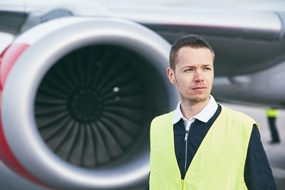 Young man looking away while standing against airplane