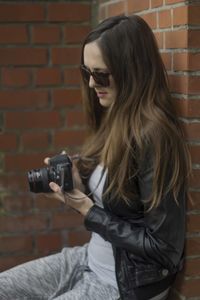 Beautiful woman photographing while leaning on brick wall