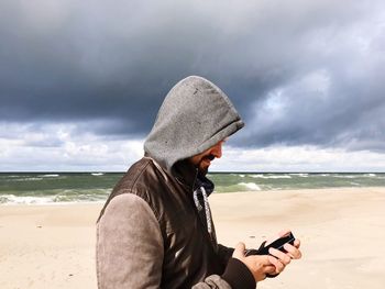 Side view of man using mobile phone at beach against sky