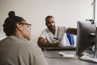 Male healthcare worker discussing over computer with female patient in medical clinic