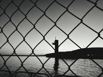 Sea seen through chainlink fence against sky during sunset