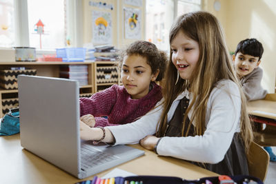 Schoolgirls using laptop together at desk in classroom