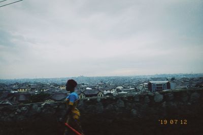 Rear view of man looking at cityscape against sky