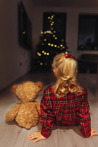 Rear view of girl sitting with teddy bear at home