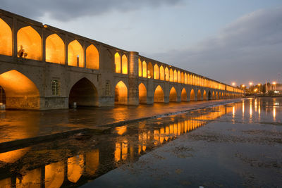 Arch bridge over river against sky during sunset