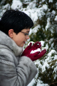 Woman in a gray fur coat with red gloves holds snow in her hands.