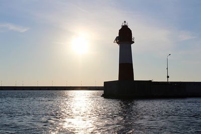 Lighthouse by sea against sky during sunset