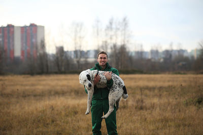 Portrait of man with dog while standing on land against sky