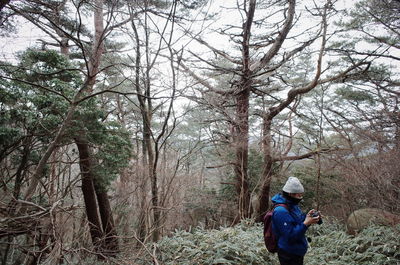 Rear view of man amidst trees in forest during winter