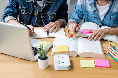 Midsection of people reading book by laptop on table