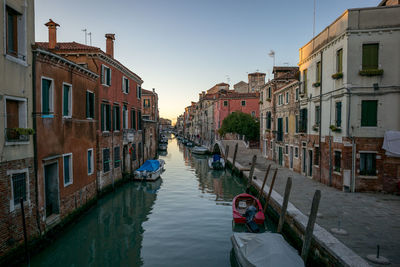 Boats moored in canal amidst buildings against clear sky