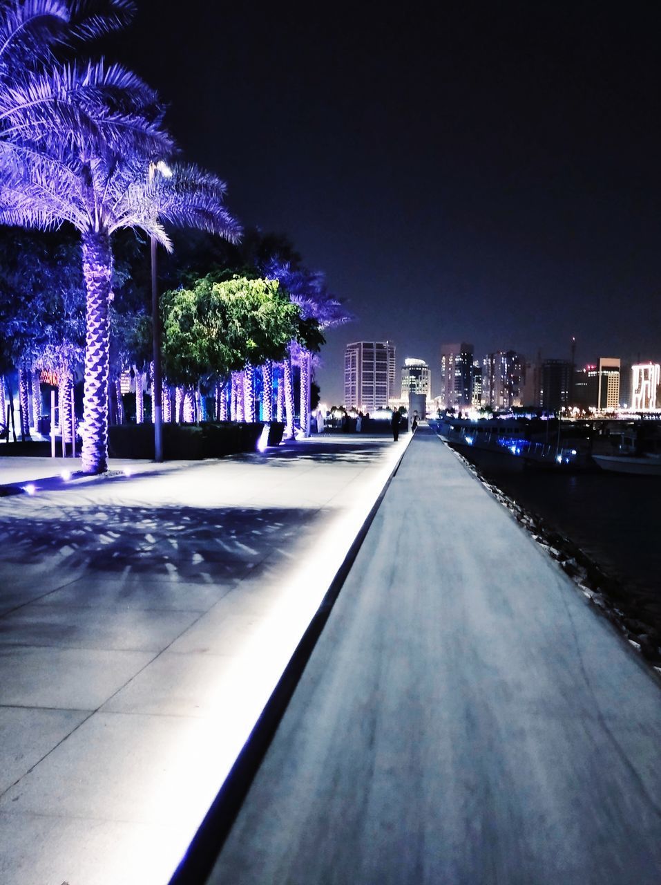 ILLUMINATED ROAD AMIDST BUILDINGS AGAINST SKY AT NIGHT