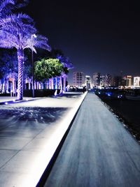 Illuminated street amidst buildings against sky at night