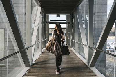 Businesswoman looking away holding bag while walking on footbridge