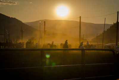 Cowboys and horses at ranch against sky during sunset
