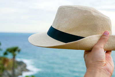 Midsection of person holding hat against sea