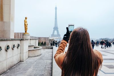 Rear view of woman photographing tower against sky