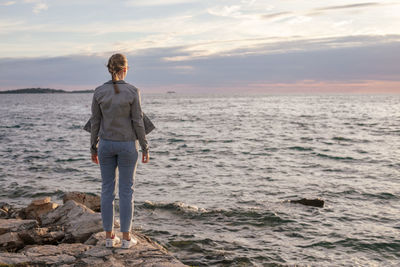 Back view of young woman standing on the stone pier lokking at the sea