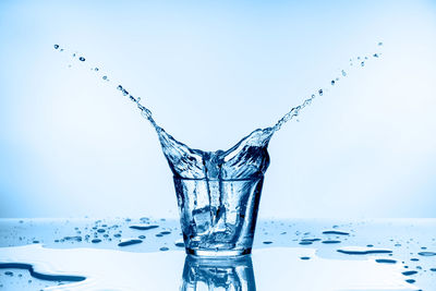 Close-up of water splashing on glass against blue background