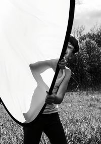 Midsection of kid holding transparent sheet while standing on field