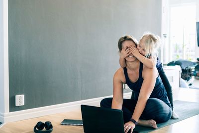 Playful daughter closing mother's eyes in living room