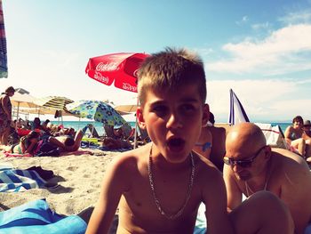 Shirtless boy with mouth open looking away while sitting at beach during summer