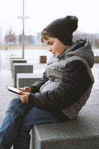 Boy using digital tablet while sitting on seat during winter