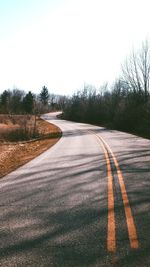 Empty road by bare trees against clear sky