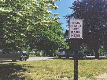 Warning sign on grassy field against parked cars by trees