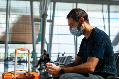 Young man wearing a face mask looking at his phone at the airport