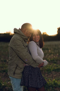 Man hugs a woman from behind in a natural landscape at sunset.
