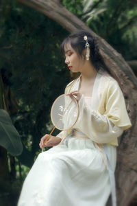 Woman wearing traditional clothing while holding hand fan in forest