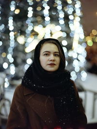 Portrait of woman standing against illuminated defocused lights