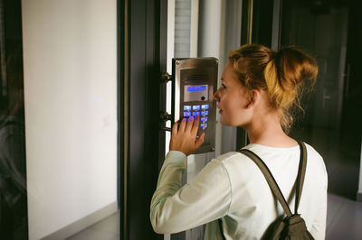 Rear view of teenage girl typing number on device at building entrance