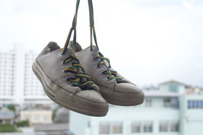 Canvas shoes hanging in city against sky