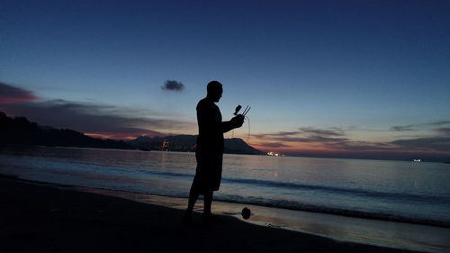 Silhouette woman standing at beach against sky during sunset