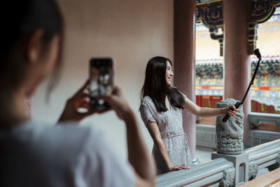 Woman holding camera while sitting in kitchen