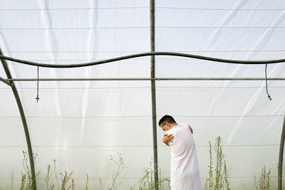 Side view of young man standing against white wall