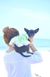 Rear view of woman with dog standing at beach