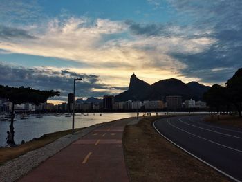 Empty road by city against sky at sunset