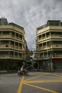 Vehicles on road by buildings against sky in city