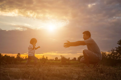 Side view of father gesturing towards daughter on land against sky during sunset