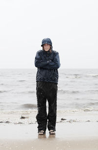 Portrait of woman wearing raincoat standing at sea shore during rainy season