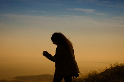 Rear view of woman against sky during sunset