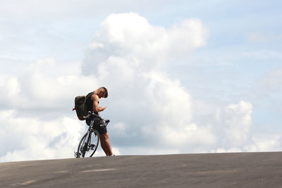 Side view of man riding bicycle against cloudy sky