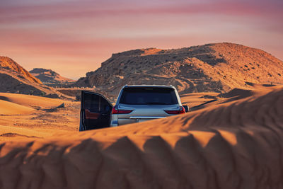 Car on desert against sky during sunset